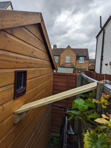 Wooden extension platform connecting two buildings, surrounded by fences and cloudy sky.