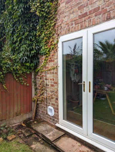 Double glass doors on a brick wall, with green ivy and a garden visible beyond.